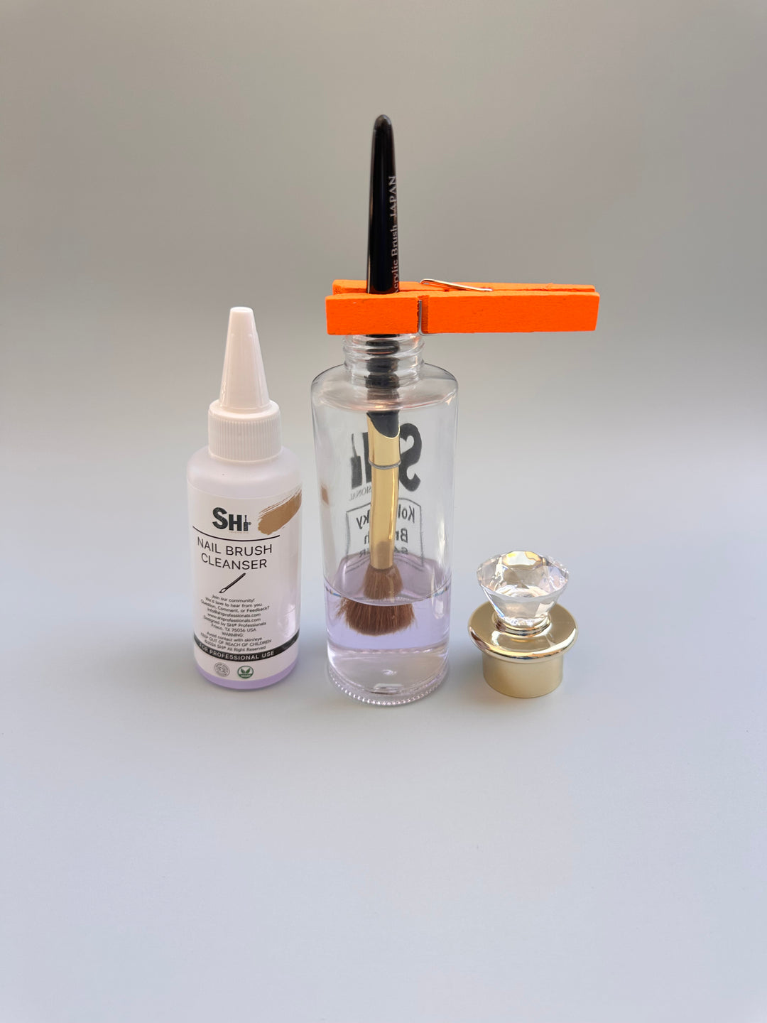 The image shows a Kolinsky acrylic brush saver kit which includes a brush, a bottle with liquid, a nail brush cleaner liquid, and a clip, displayed on a white surface.