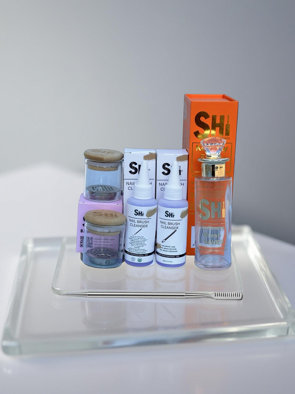 Collection of nail brush care products on a glass tray with a gray background